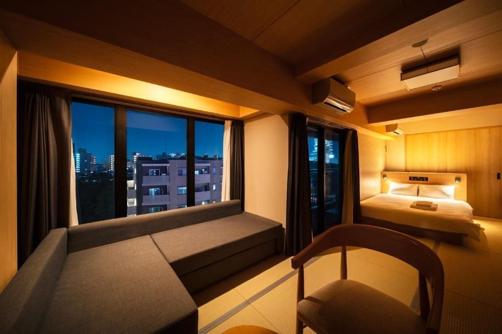 Habitación de hotel con cama, sofá, sillón y vista a la ciudad de noche.