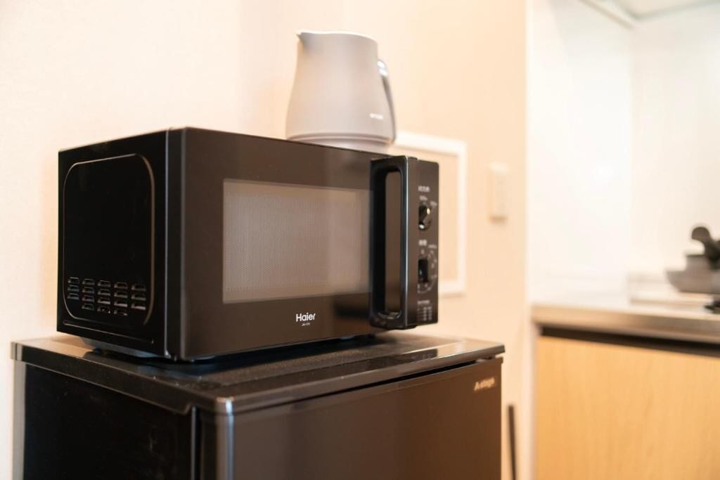 A black microwave oven with a coffee maker on top, placed on a black refrigerator in a kitchen.
