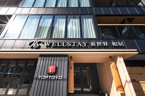 Entrada de hotel con señalización que indica 'WELLSTAY' y 'TOPTOYO'.