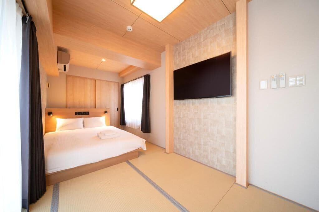 Une chambre d’hôtel équipée d’un lit, d’un téléviseur à écran plat fixé au mur, d’un luminaire au plafond et d’une fenêtre avec des rideaux.