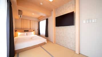 Une chambre d’hôtel équipée d’un lit, d’un téléviseur à écran plat fixé au mur, d’un luminaire au plafond et d’une fenêtre avec des rideaux.
