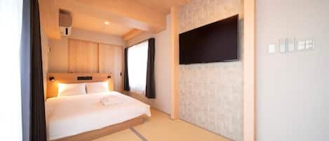 A hotel room with a bed, a flat-screen TV mounted on the wall, a ceiling light, and a window with curtains.