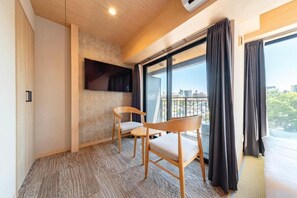 Habitación de hotel con un ventanal grande, un televisor de pantalla plana en la pared y dos sillas de madera.