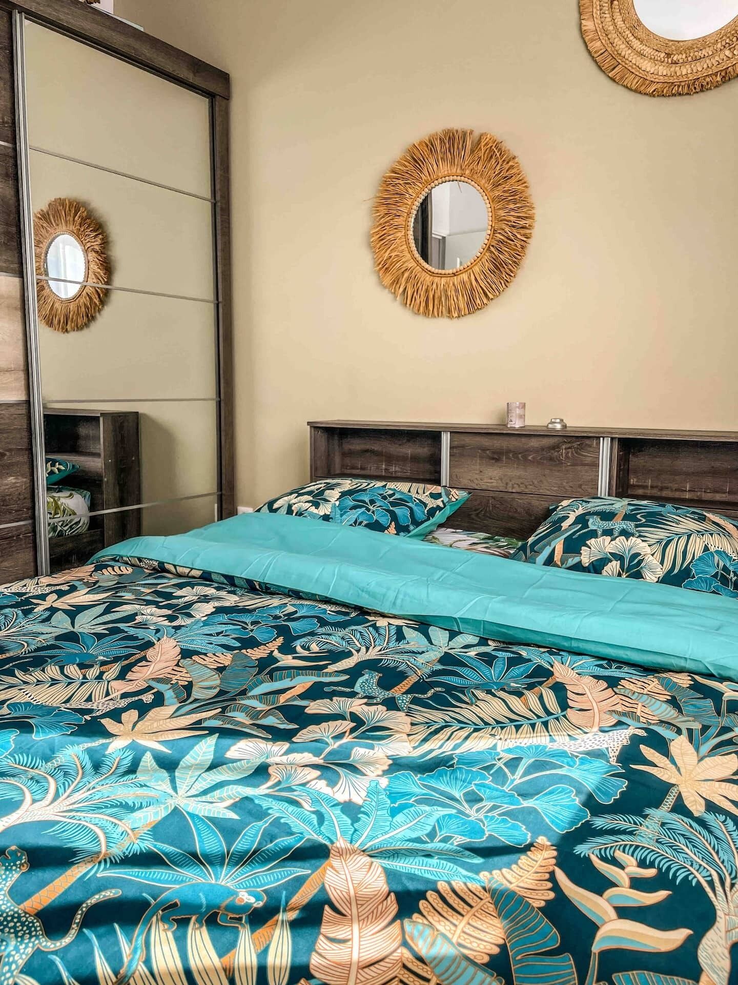 Un dormitorio con cama, dos espejos redondos, cabecero de madera y mesita de noche con una vela.