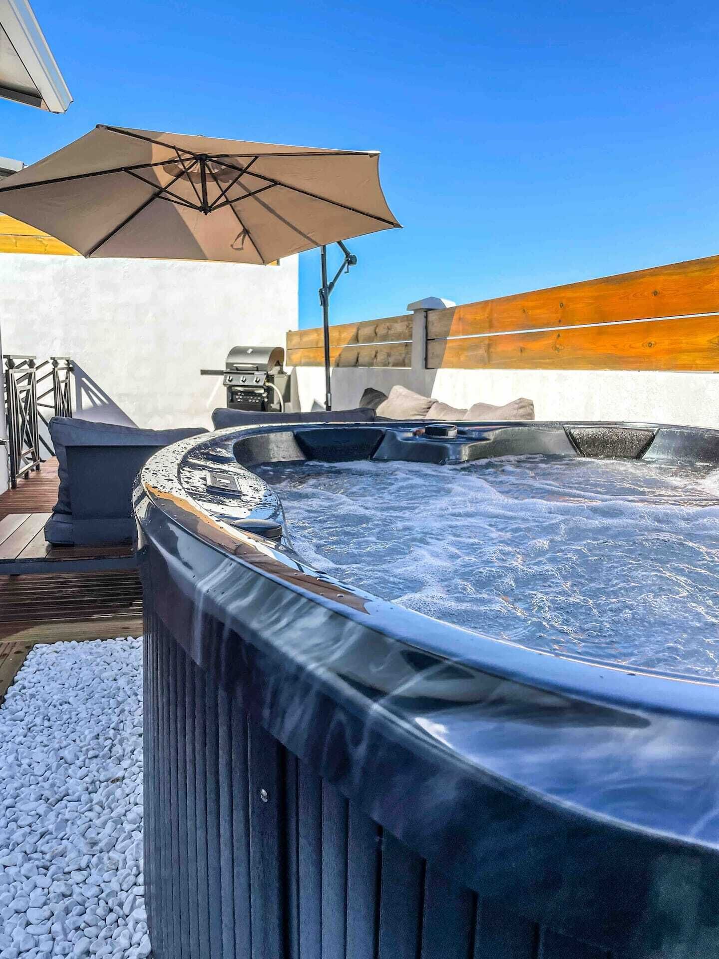 Een hottub met een houten terras en een zonnescherm.