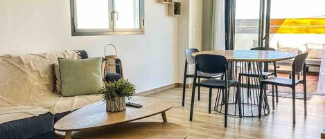 A modern living room with a sofa, a coffee table, and a dining area with chairs and a table.