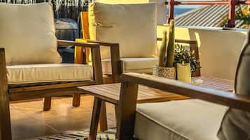 Un espacio exterior iluminado por el sol con un sofá blanco, una mesa de madera y una alfombra estampada.