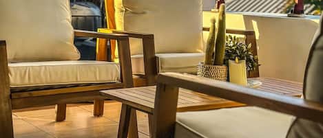 A sunlit outdoor seating area with a white sofa, a wooden table, and a patterned rug.