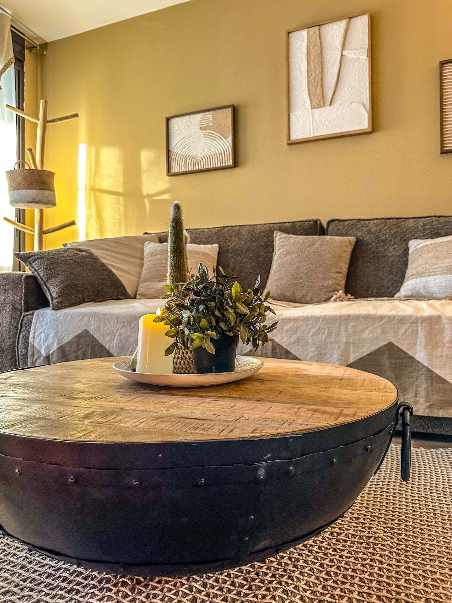 Un salon avec une table basse ronde, un cactus, une bougie et une plante en pot.