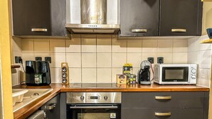 Una cucina con mobili scuri, una cappa aspirante in acciaio inossidabile, un forno a microonde, una macchina da caffè e un tostapane.