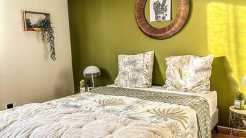 Un dormitorio con cama, un adorno circular en la pared, una mesita de noche con lámpara y una planta colgante.
