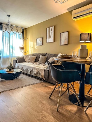 A modern living room with a sofa, a dining table with chairs, and artwork on the walls.