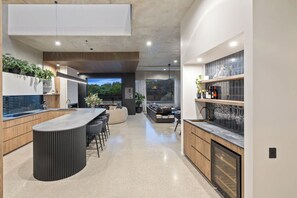 A modern kitchen with a bar area, built-in appliances, and a large window providing a view of the outdoors. - Black on Black Wattle - Beachfront, Rooftop, Pool (Casuarina)