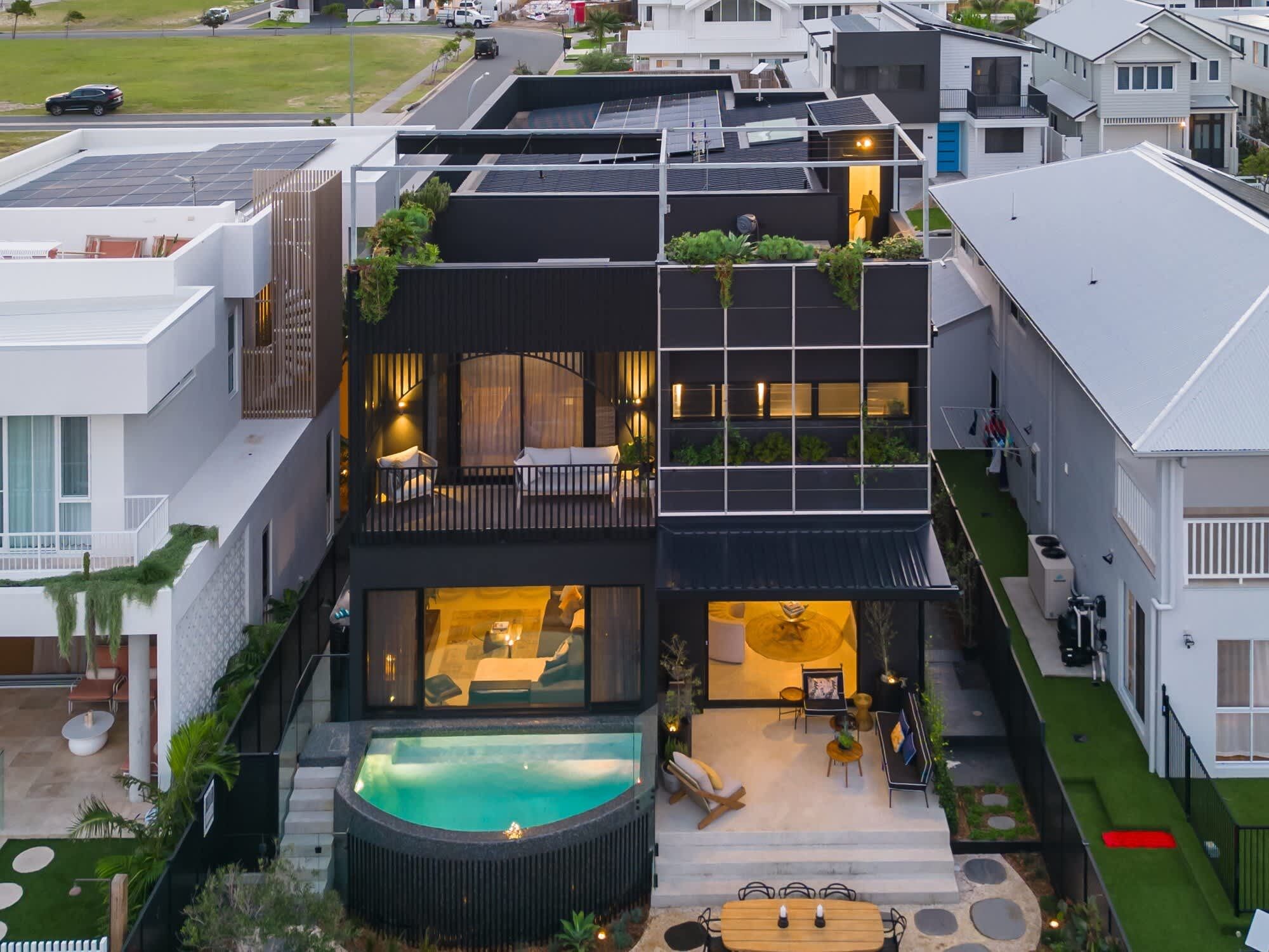 A modern multi-story house with a rooftop garden, a swimming pool, and a covered outdoor seating area.