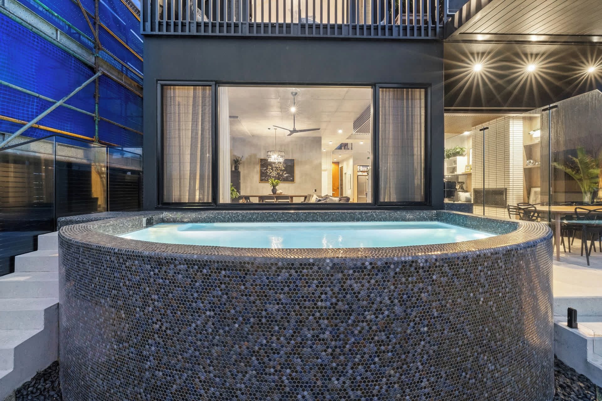 Un moderno jacuzzi exterior con diseño de mosaico, rodeado por un muro de piedra y escalones.