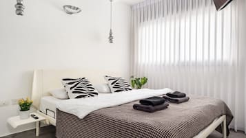 A modern bedroom with a bed, bedside table, and a window with sheer curtains.