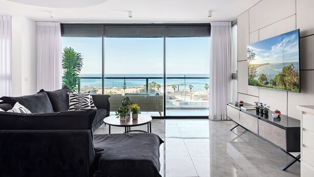 Een moderne woonkamer met een grote televisie, een bank, een salontafel en uitzicht op het strand.