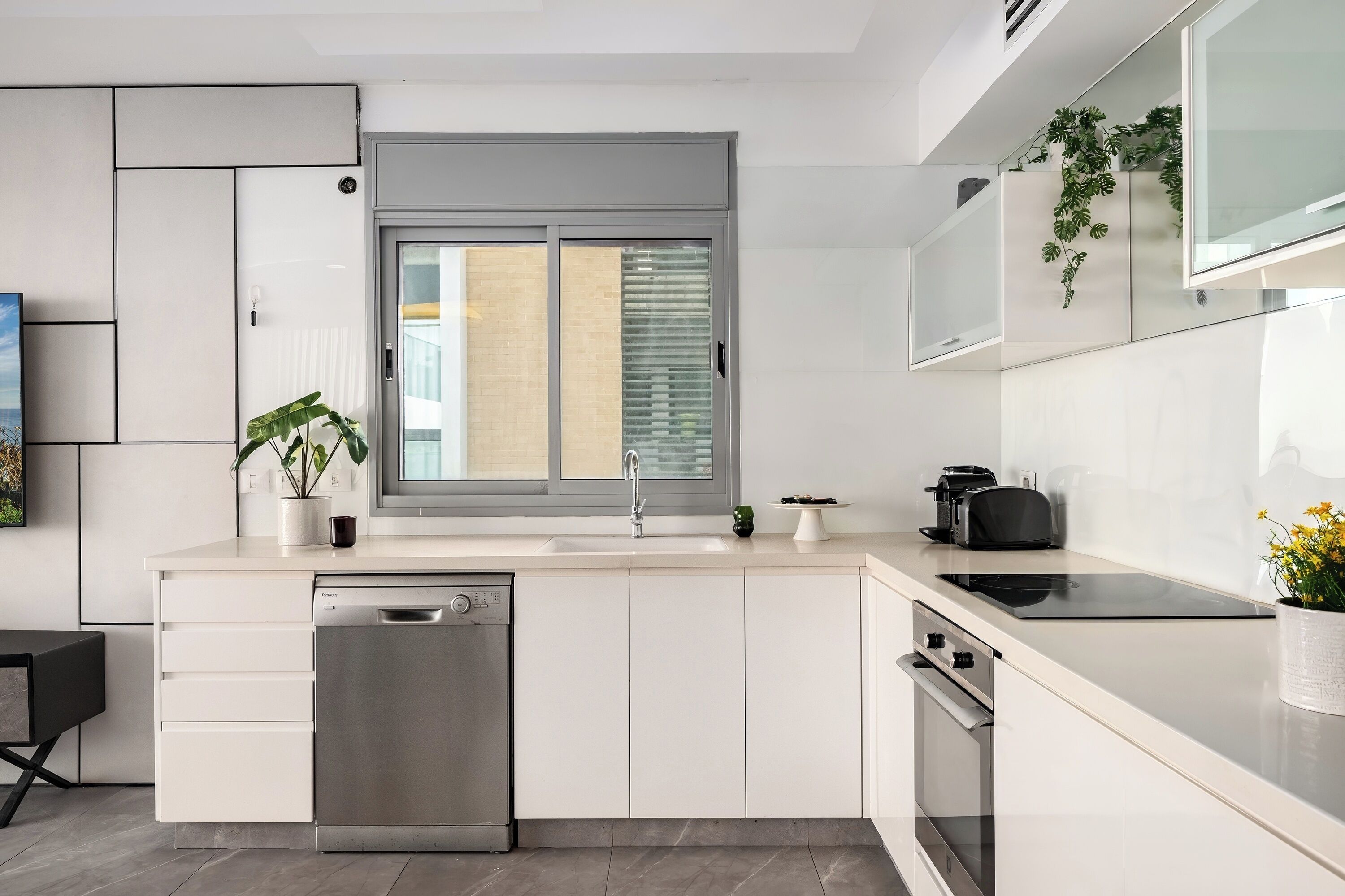 A modern kitchen with a dishwasher, oven, and a window with blinds.
