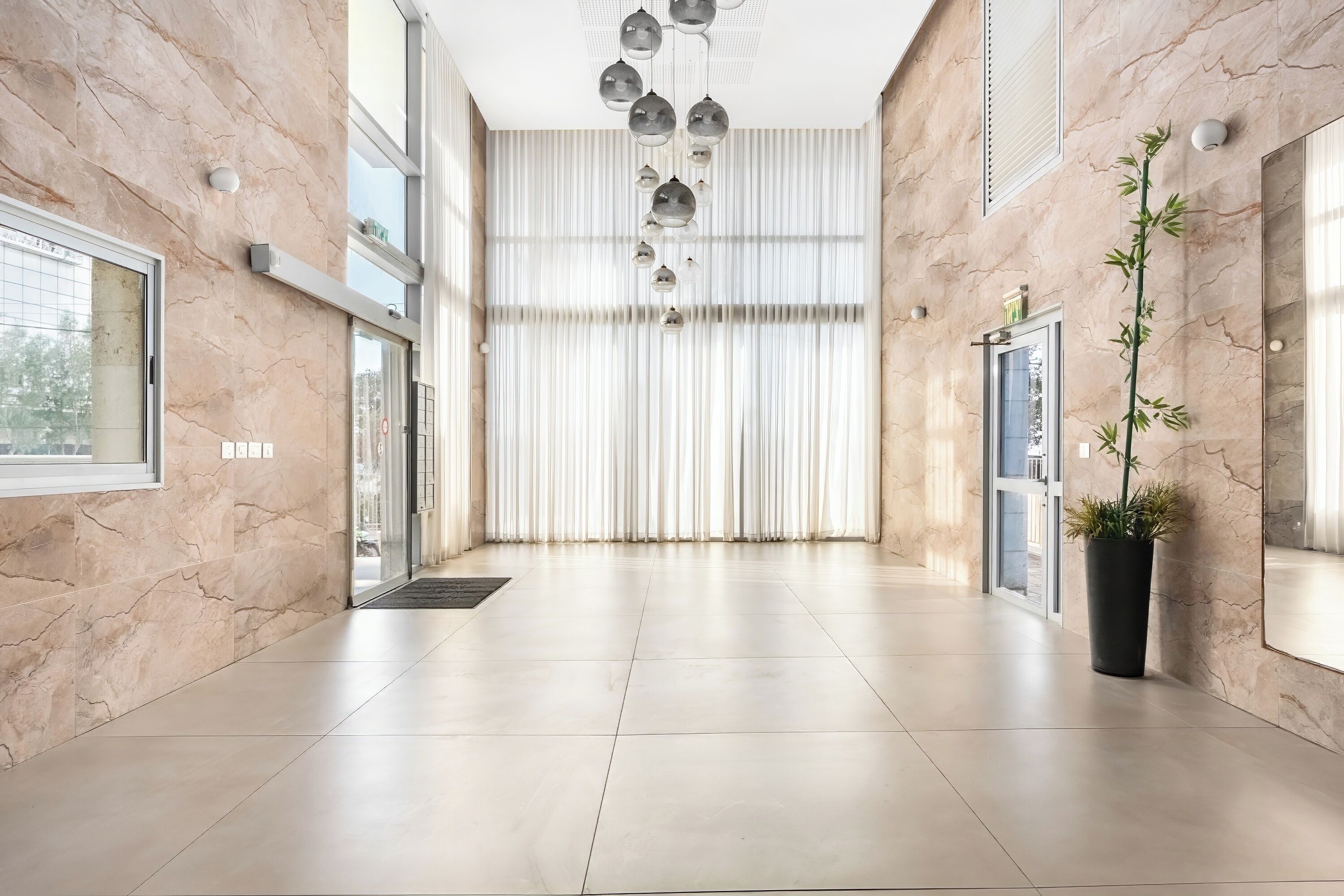 A spacious lobby with marble walls, a modern chandelier, large windows, and a potted plant.