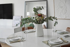 Ein Esstisch ist gedeckt mit Tellern, Besteck und einer Vase mit Blumen.