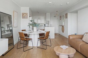 Eine moderne Küche mit weißen Schränken, einem Esstisch mit Stühlen und einem Wohnbereich mit braunem Sofa und rundem Holztisch.