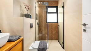 A modern bathroom with a glass shower enclosure, a white sink, and a wooden vanity. - Stylish 2BR City Apartment Near the Beach & Bograshov (Tel Aviv-Yafo)