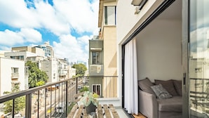 A balcony with a wooden table, a potted plant, and a sofa with cushions. - Stylish 2BR City Apartment Near the Beach & Bograshov (Tel Aviv-Yafo)