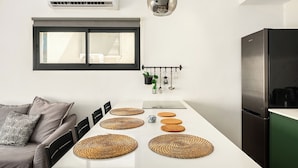 A modern kitchen with a dining table, chairs, a refrigerator, and an air conditioning unit. - Stylish 2BR City Apartment Near the Beach & Bograshov (Tel Aviv-Yafo)