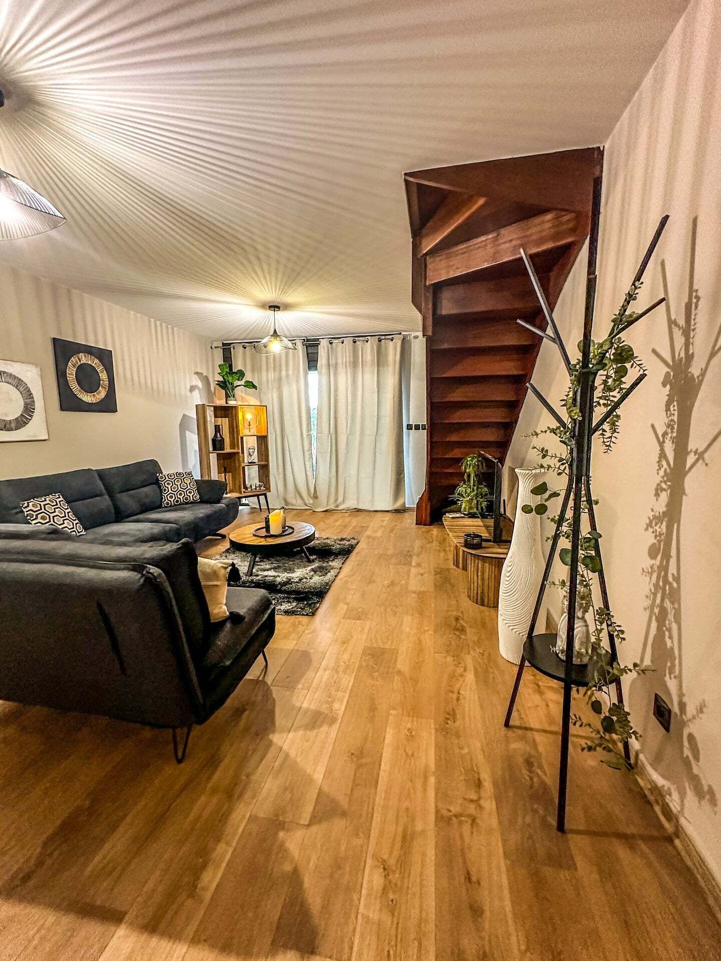 En moderne stue med en sort sofa, trægulv, trappe og en plante.