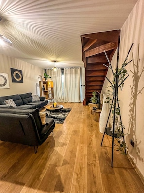 En moderne stue med en sort sofa, trægulv, trappe og en plante.