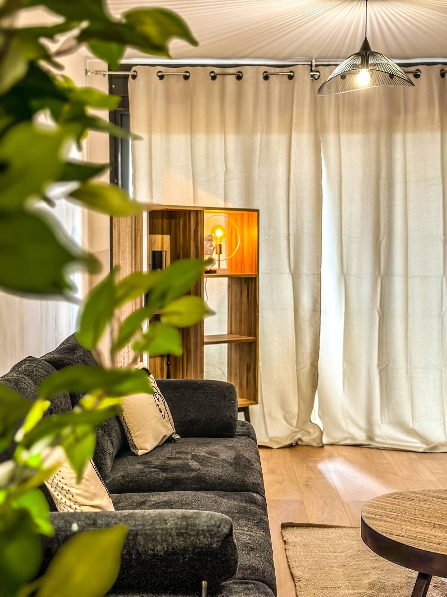 Een woonkamer met een donkergrijze bank, een rond salontafeltje en een boekenkast met een lamp.