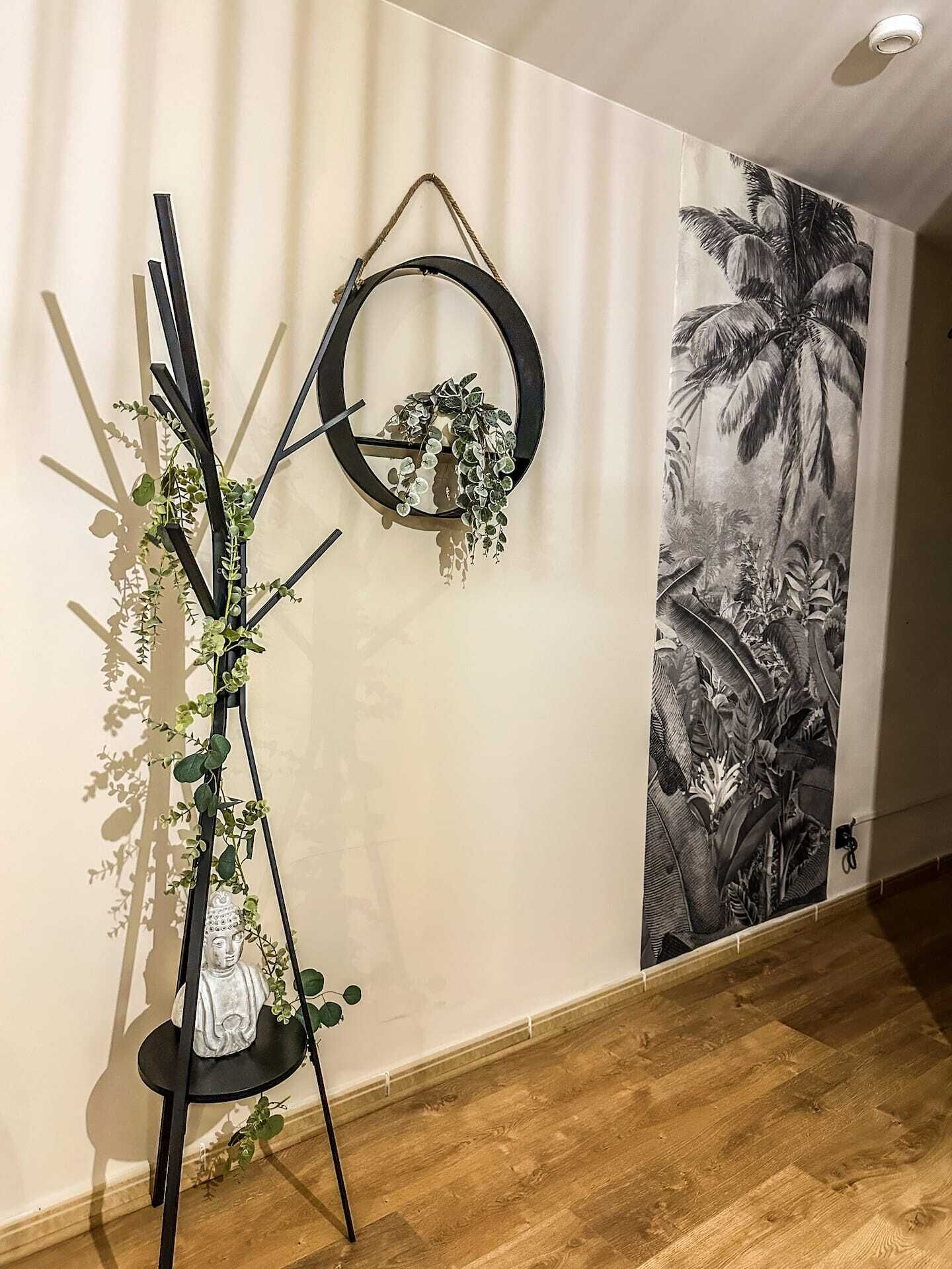 Een kamer met een houten vloer, een wandplank met groene planten en een groot zwart-wit bloemenmural.