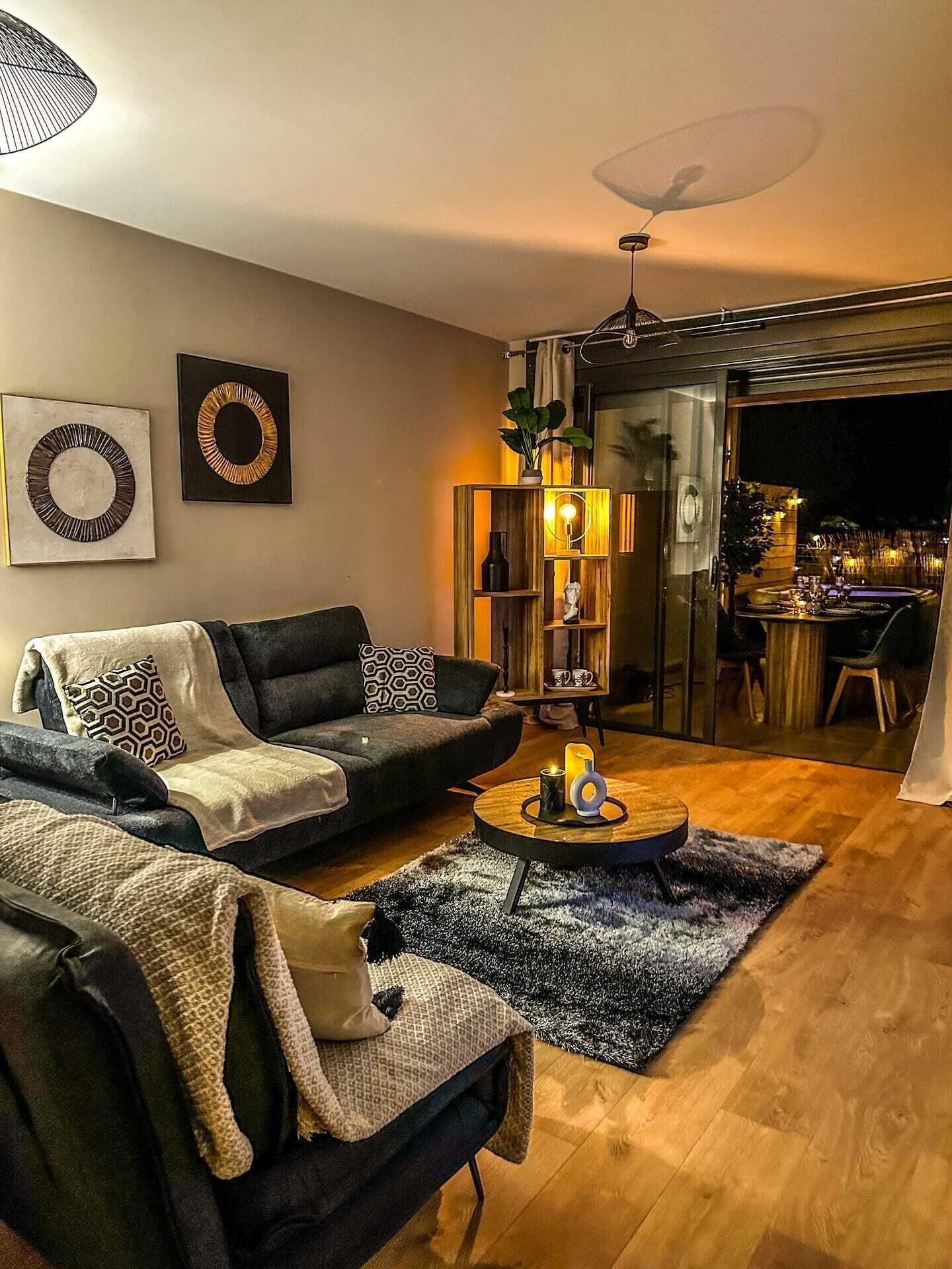 Una sala de estar moderna con un sofá modular, una mesa de centro y un área de comedor visible a través de una partición de vidrio.