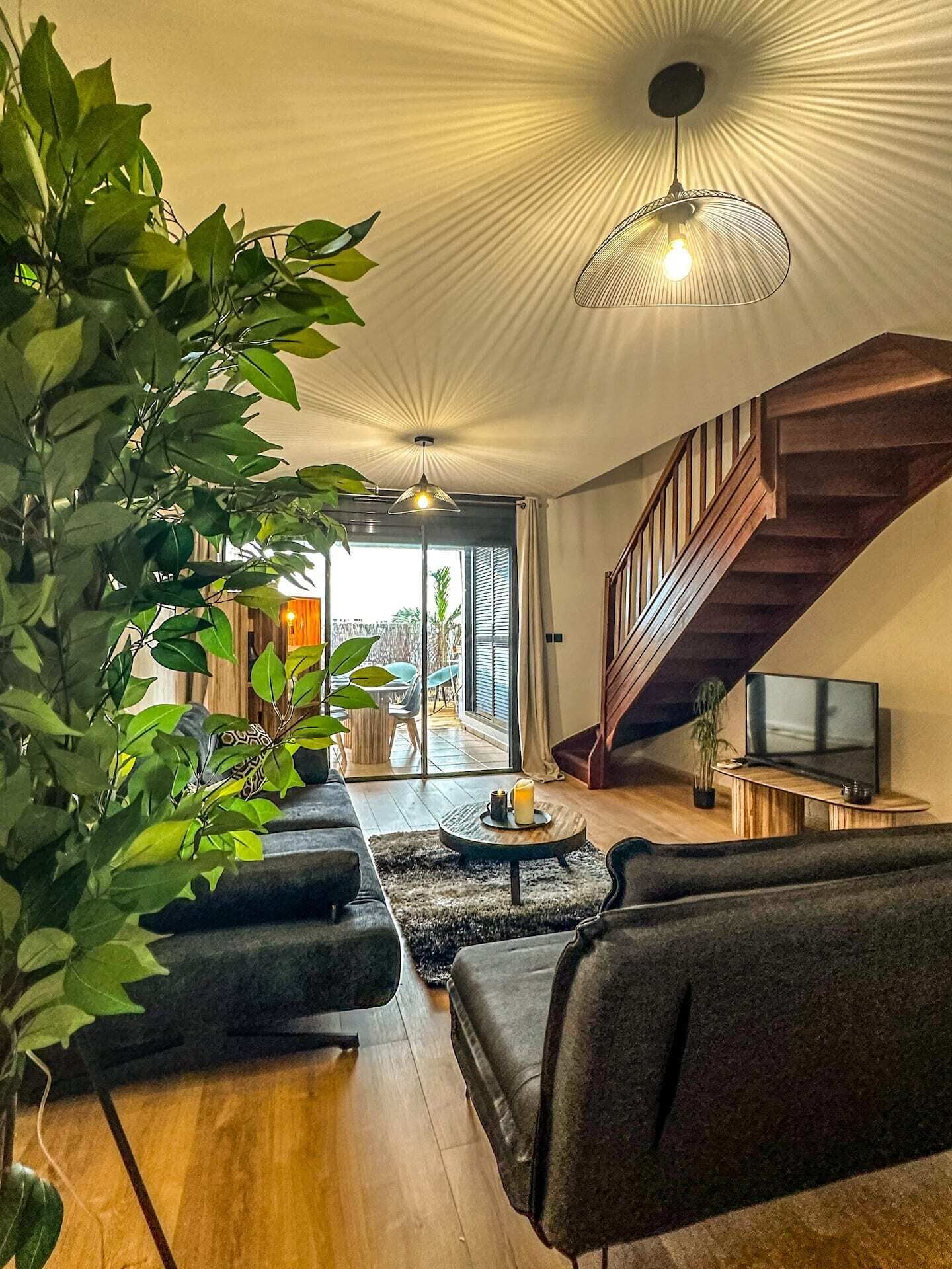 Un salon moderne avec un escalier, un téléviseur et une grande plante.