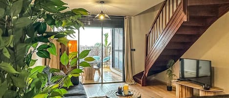 Un salon moderne avec un escalier, un téléviseur et une grande plante.