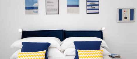 Una cama con dos almohadas, una mesita de noche con un libro y cuatro cuadros en la pared.