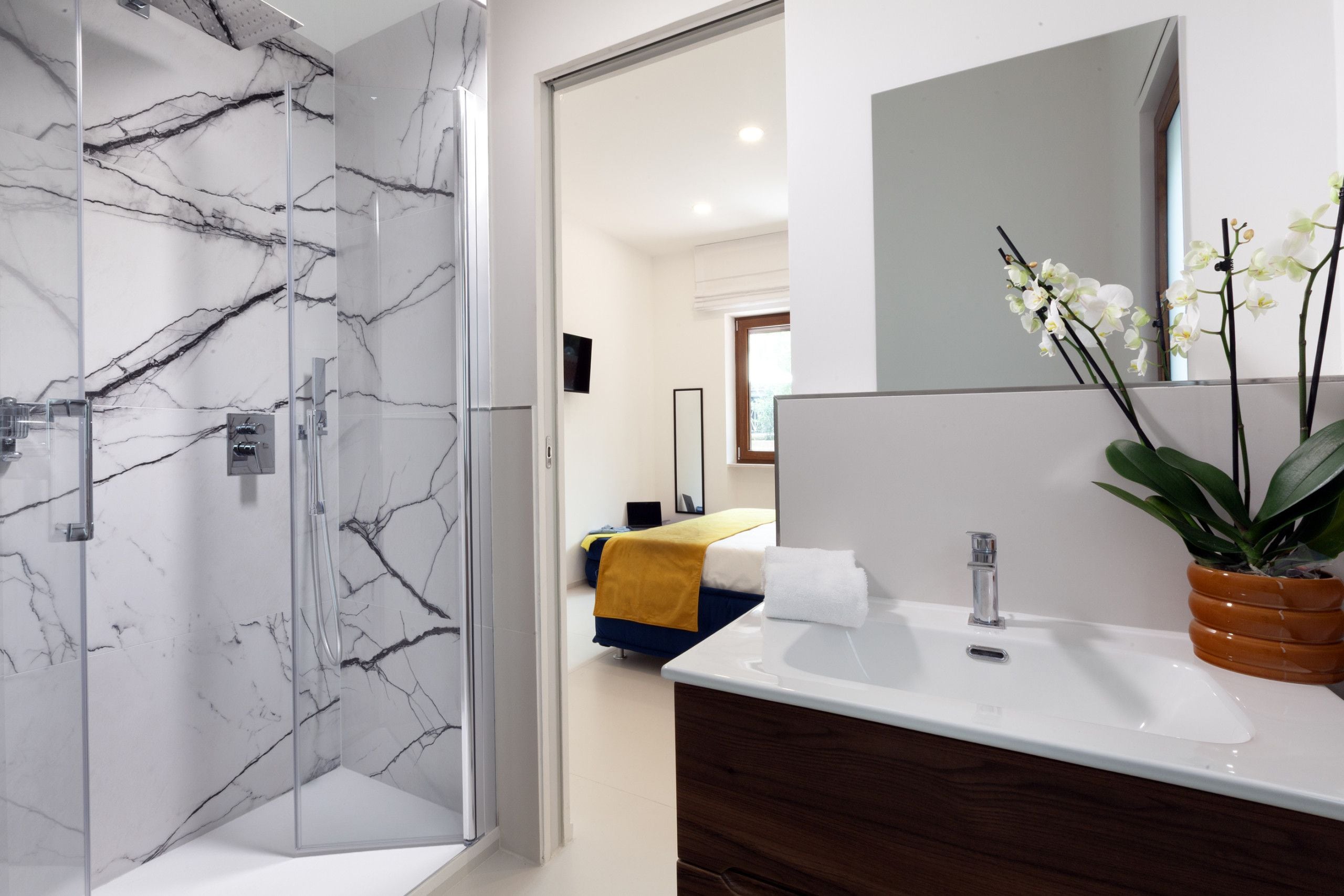 A modern bathroom with a glass-enclosed shower, a white sink with a wooden vanity, and a mirror above.