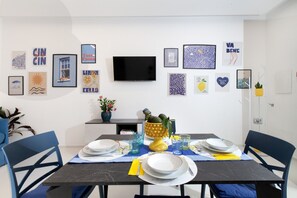 En matplats med ett bord dukat för två personer, stolar, en platt-TV som är monterad på väggen och olika inramade konstverk på väggarna.