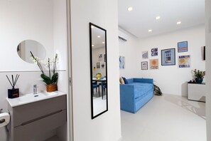 Ein modernes Wohnzimmer mit einem blauen Sofa, einer weißen Wand mit Kunstwerken und einem runden Spiegel.