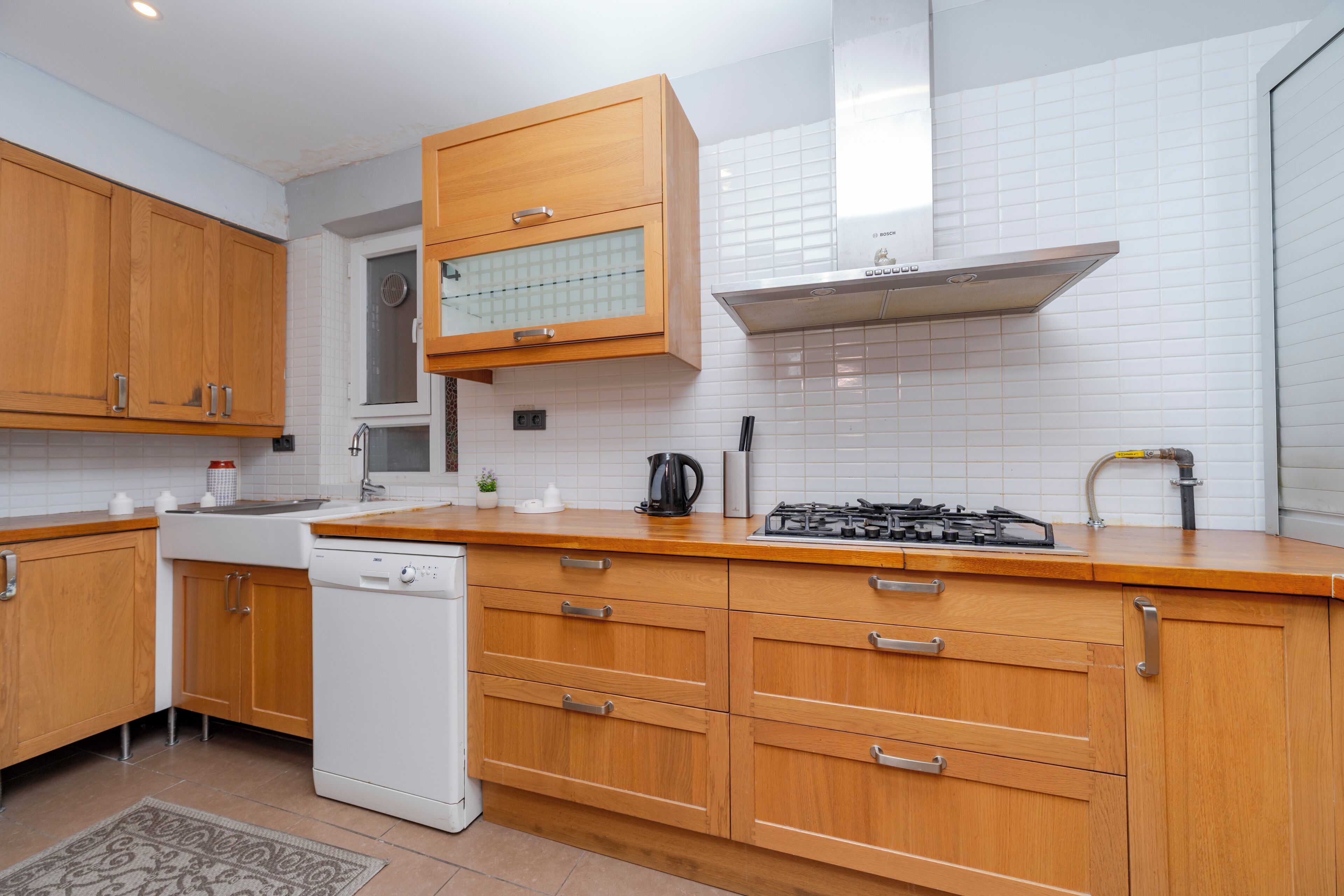 A modern kitchen with wooden cabinets, a dishwasher, a stove, and a window above the sink.