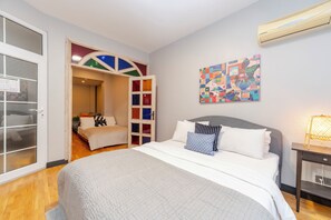 A bedroom with a bed, a nightstand, a wall-mounted air conditioner, and a colorful abstract painting. - Spacious 4BR Private Townhouse with Exclusive Terrace (İstanbul)