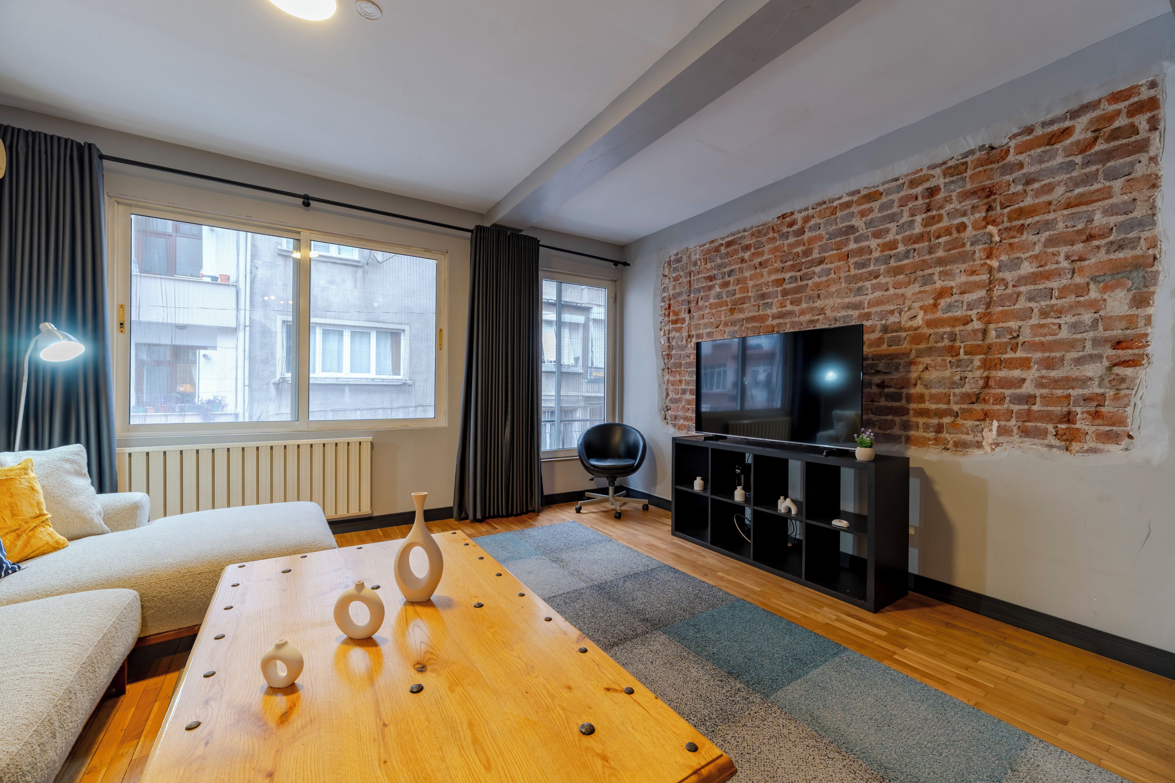A modern living room with a brick wall, a sofa, a coffee table, a TV, and a black chair.