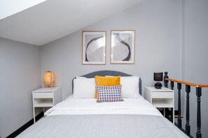 A bedroom with a bed, two bedside tables, a nightstand, a lamp, and two framed abstract artworks on the wall.