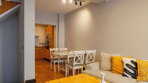 Ein modernes Wohnzimmer mit einem Holzesstisch, weißen Stühlen und einem Sofa mit gelben Kissen.