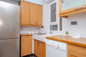 A modern kitchen with wooden cabinets, a stainless steel refrigerator, a dishwasher, and a window with a view of the outside.