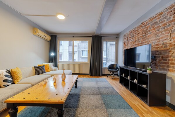 A modern living room with a sofa, coffee table, TV, and a brick wall.