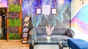 A reception area with a sofa, a glass coffee table, a bookshelf, and a decorative wall with leaf patterns. - Classic Aspiring Inn (Kolkata)
