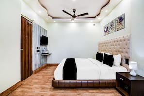 Un dormitorio con cama, ventilador de techo, televisor montado y cuadros en la pared.