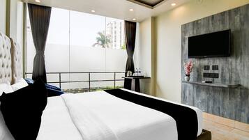 A hotel room with a large bed, a flat-screen TV mounted on a wooden wall, and a balcony with a view of buildings.