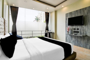 Habitación de hotel con una cama grande, un televisor de pantalla plana montado en una pared de madera y un balcón con vistas a edificios.